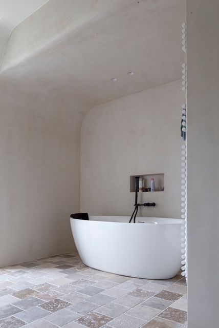 Moderne, minimalistische badkamer met een wit vrijstaand bad en een vloer van natuurstenen tegels.