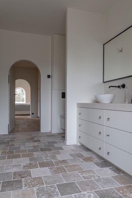 Moderne badkamer met wit badmeubel, boogvormige deuropening en tegelvloer met patroon.
