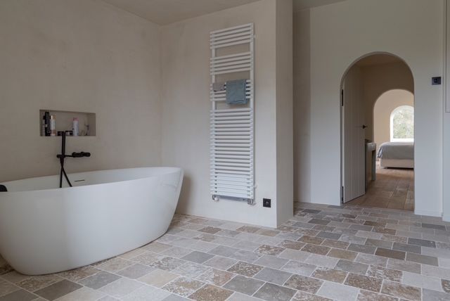 Ruime, moderne badkamer met vrijstaand bad, tegelvloer en uitzicht op de gewelfde gang.