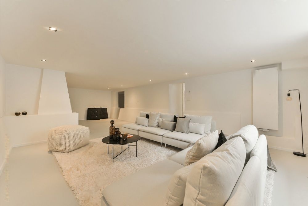 Lichte, moderne, witte woonkamer met hoekbank, fauteuil, salontafel en open haard.