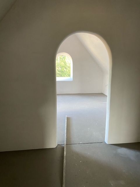 Lege kamer met een boogvormige deuropening en een klein boogvormig raam dat daglicht binnenlaat.