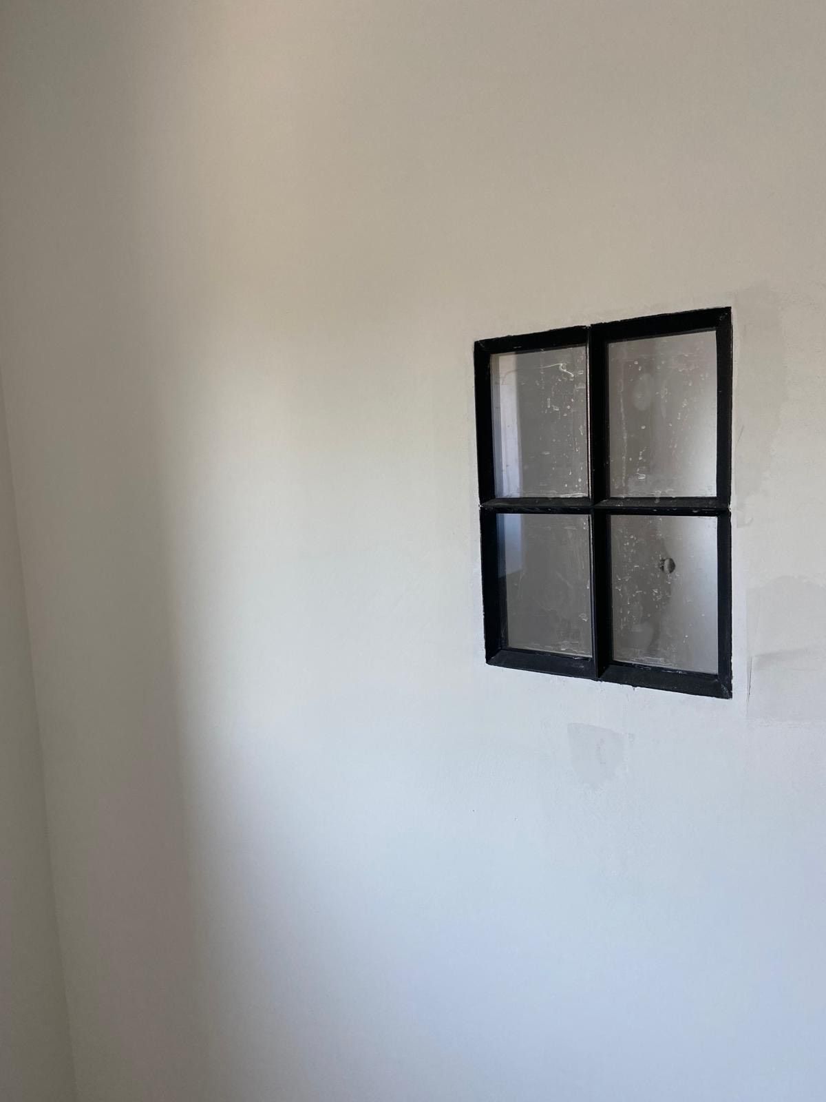 Witte muur met een klein raam met vier ruiten en een zwart frame.