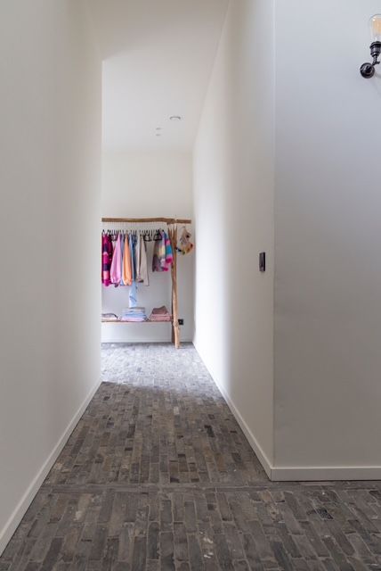 Smalle witte gang met grijze tegelvloer die leidt naar een open kast vol kleding.