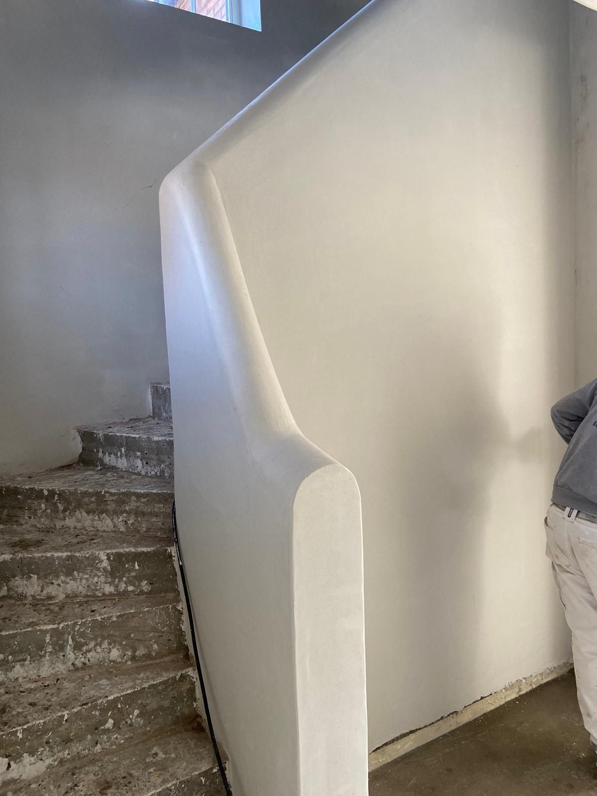 Trappenhuis met betonnen treden en een witte gebogen muur of leuning in een smalle gang.