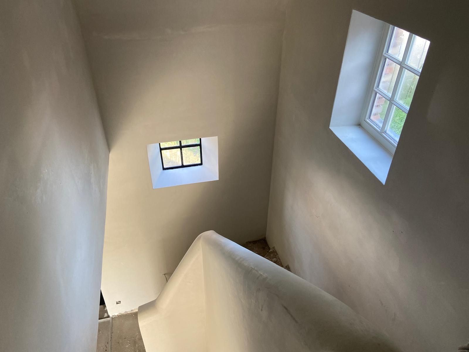 Uitzicht op een beige trappenhuis met twee kleine ramen die daglicht binnenlaten.