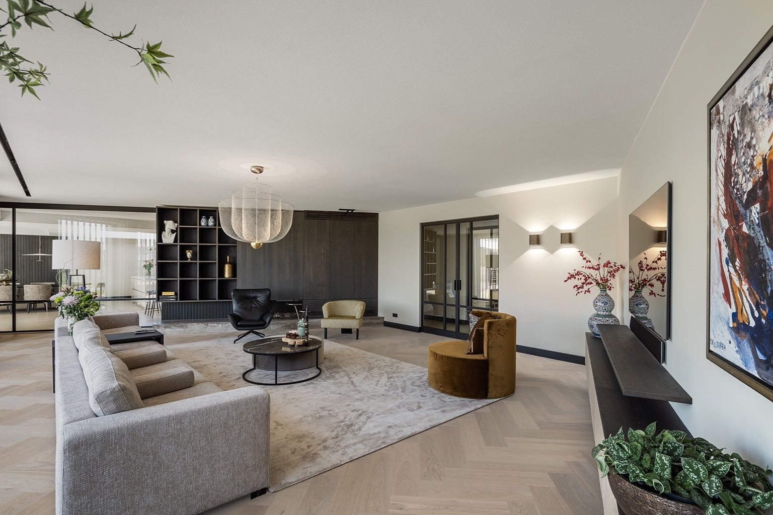 Moderne woonkamer met grijze hoekbank, zwarte stoelen, kroonluchter, open haard en kunst aan de muur.