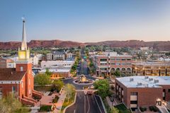 Aerial view of a city street lined with buildings and a church with a tall steeple, set against red rock mountains.