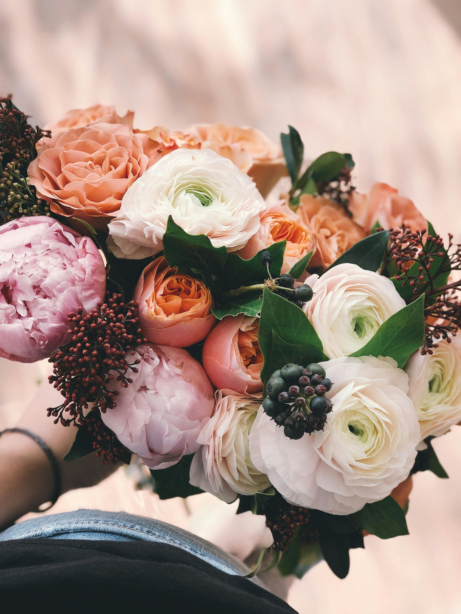 Close-up of a bouquet with pink, peach, and white flowers, including peonies and ranunculus.