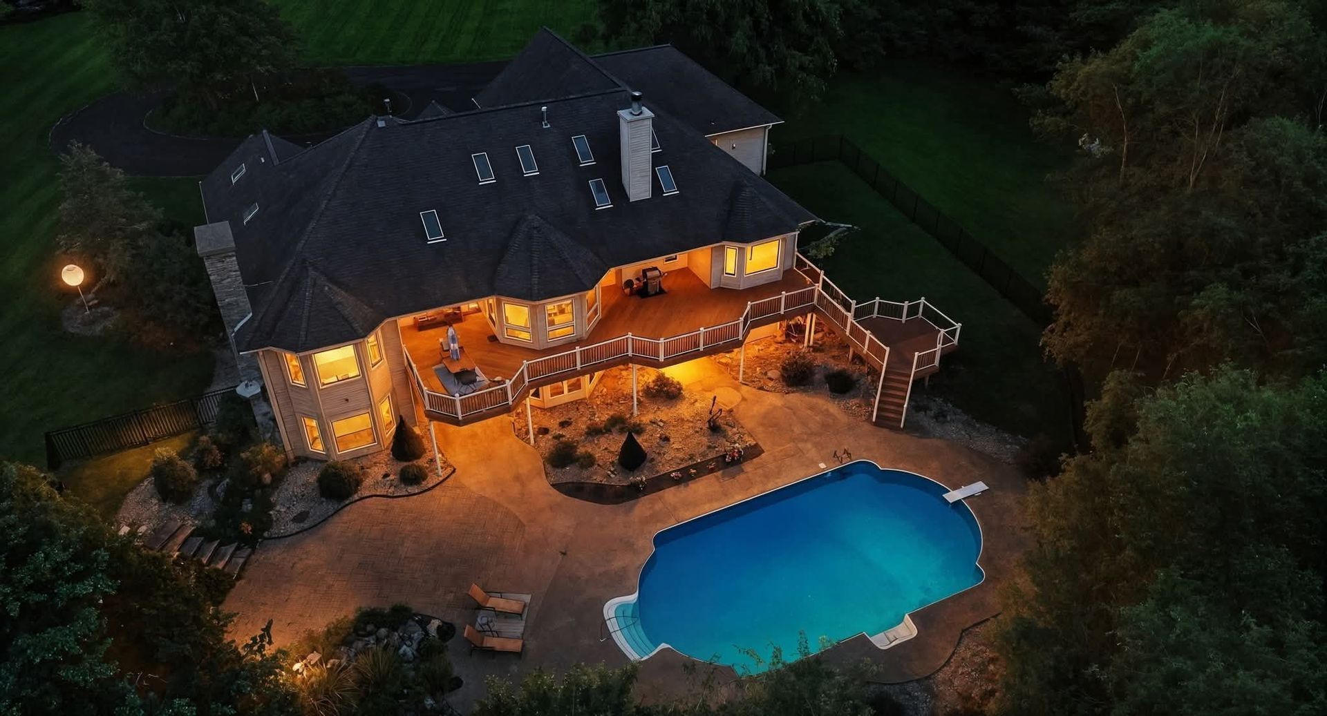 Evening aerial drone presentation of a home with an illuminated deck and pool