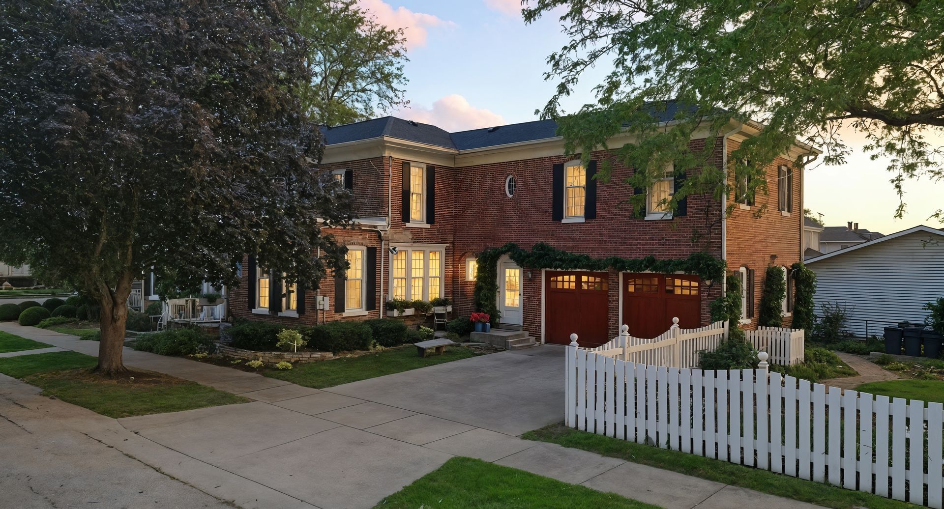 Evening presentation of a brick home beside a driveway and white fence