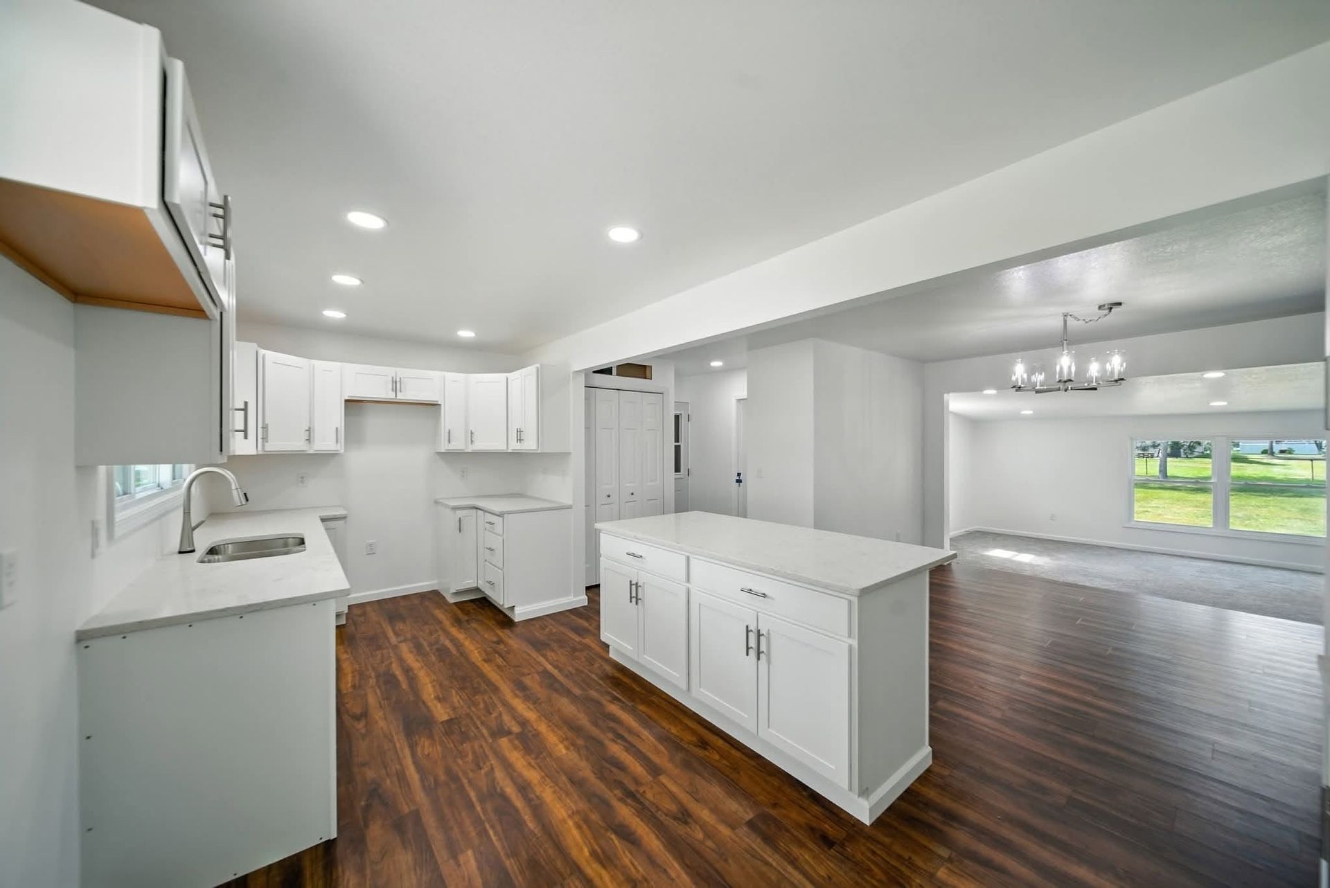 Unfurnished open-plan kitchen with a white island and dark wood flooring