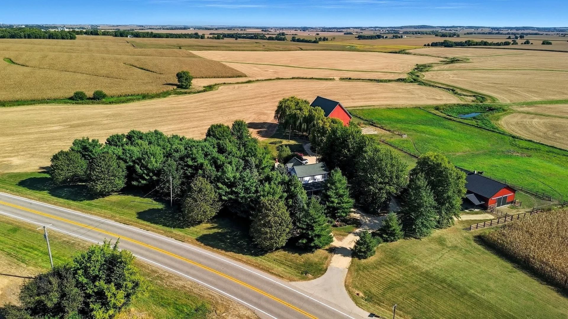 Aerial drone view of a rural property with trees, outbuildings and surrounding fields