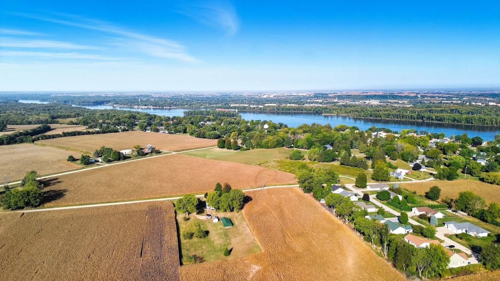 Wide aerial drone view of farmland, residential streets and water in the distance