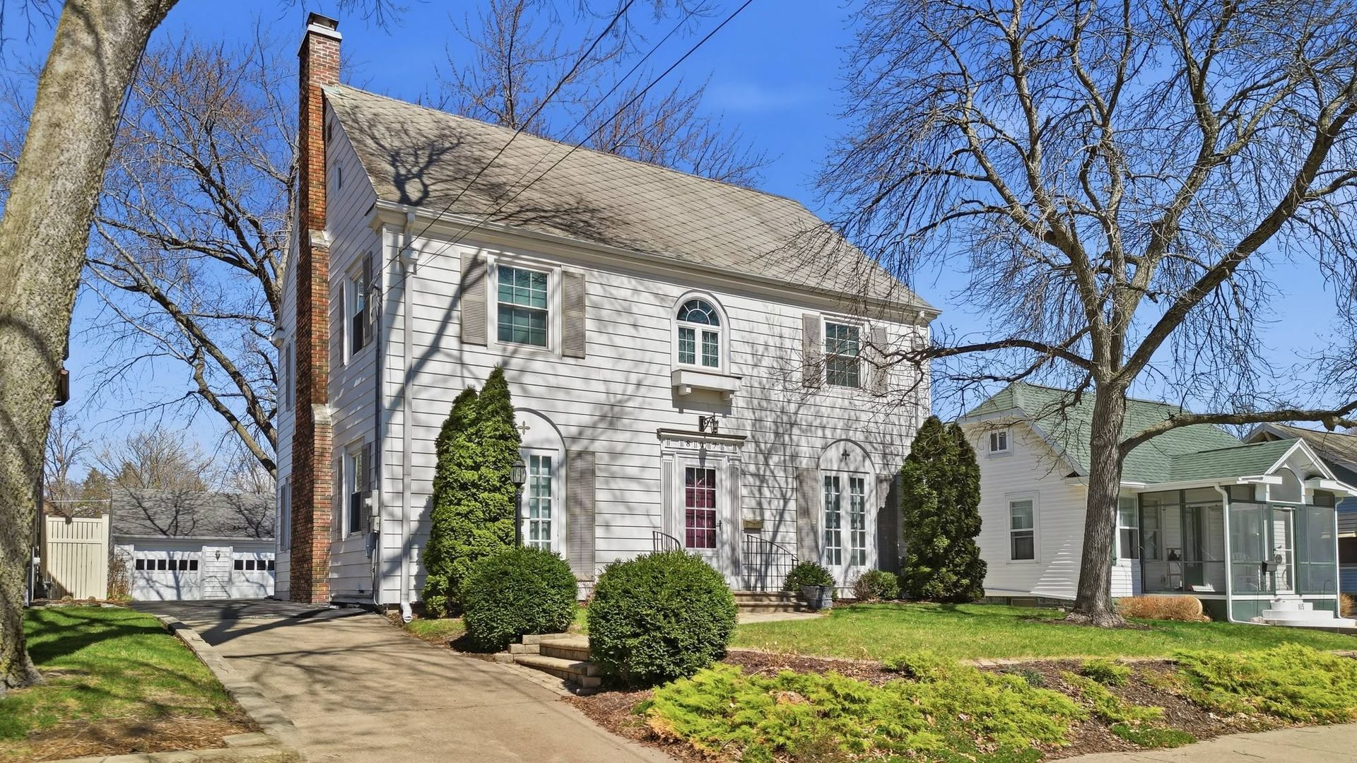 White two-story home with dark shutters and a landscaped entrance