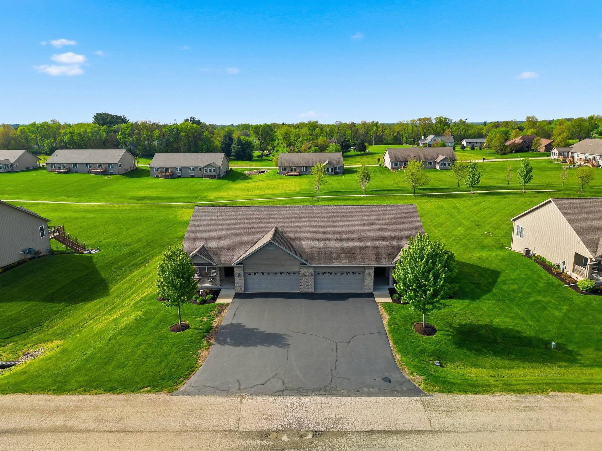 Aerial drone view of a single-story home with an attached garage and front lawn