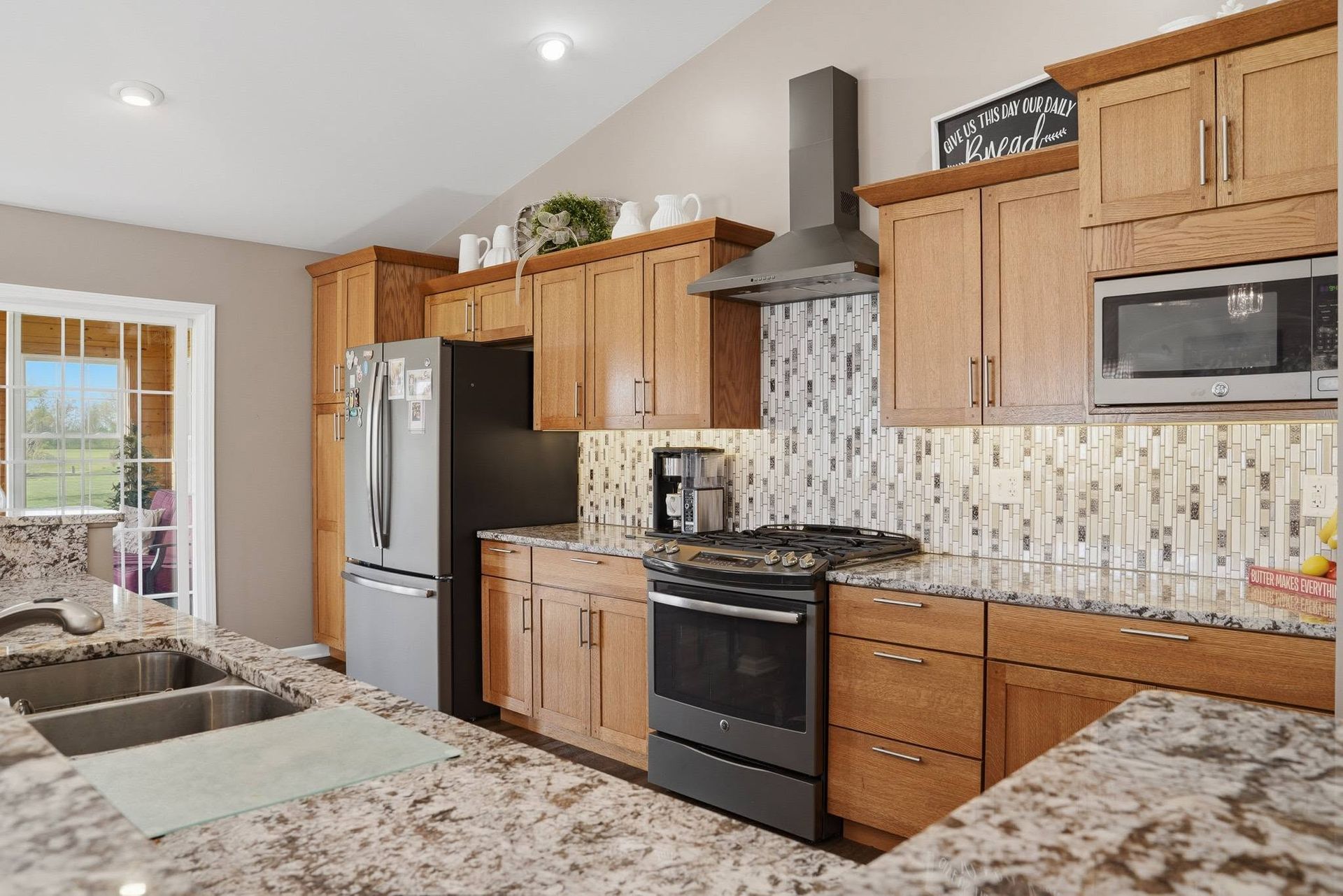 Kitchen with light wood cabinets, patterned backsplash and dark appliances