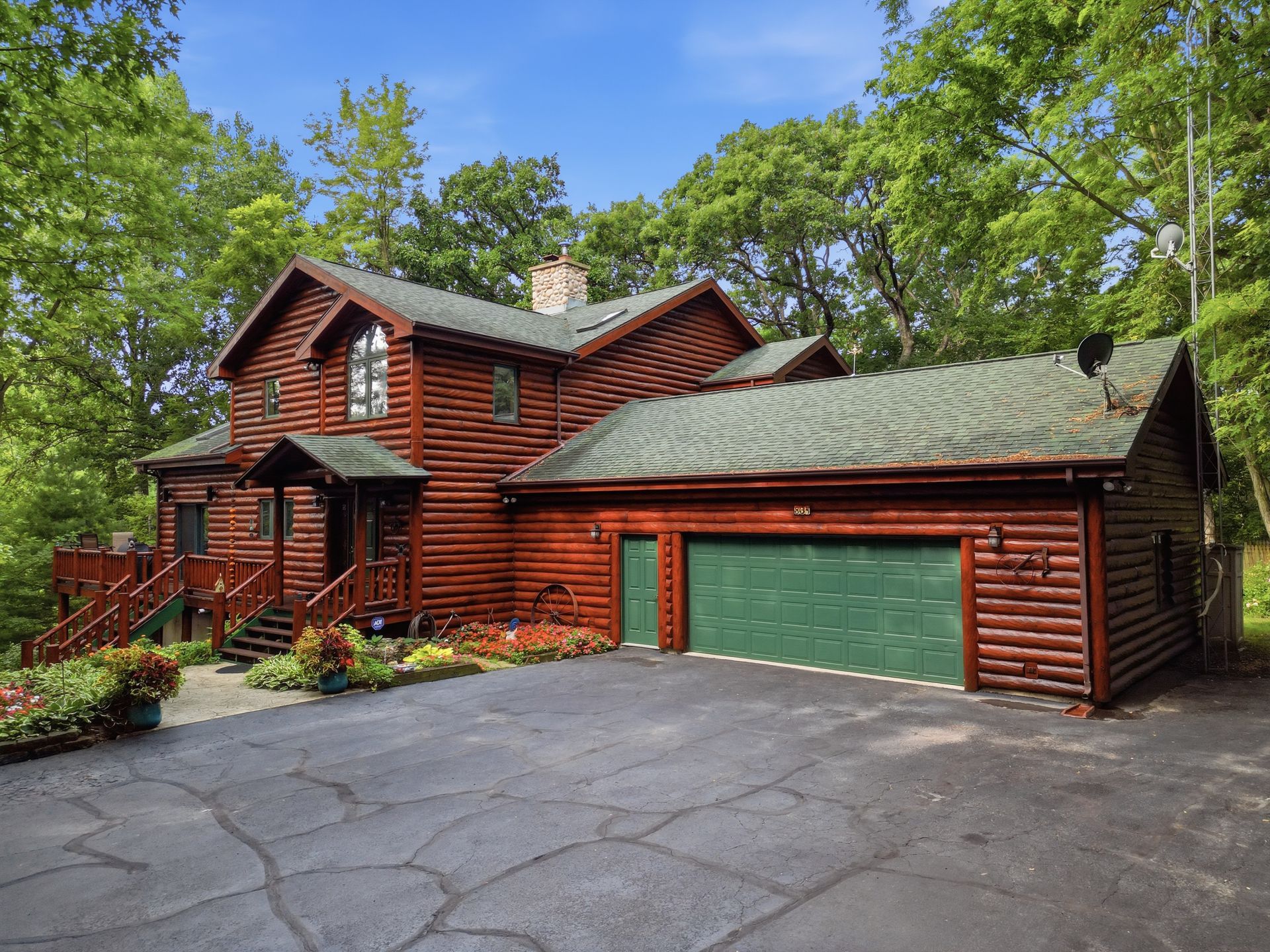 Log home with an attached garage beside a wooded driveway