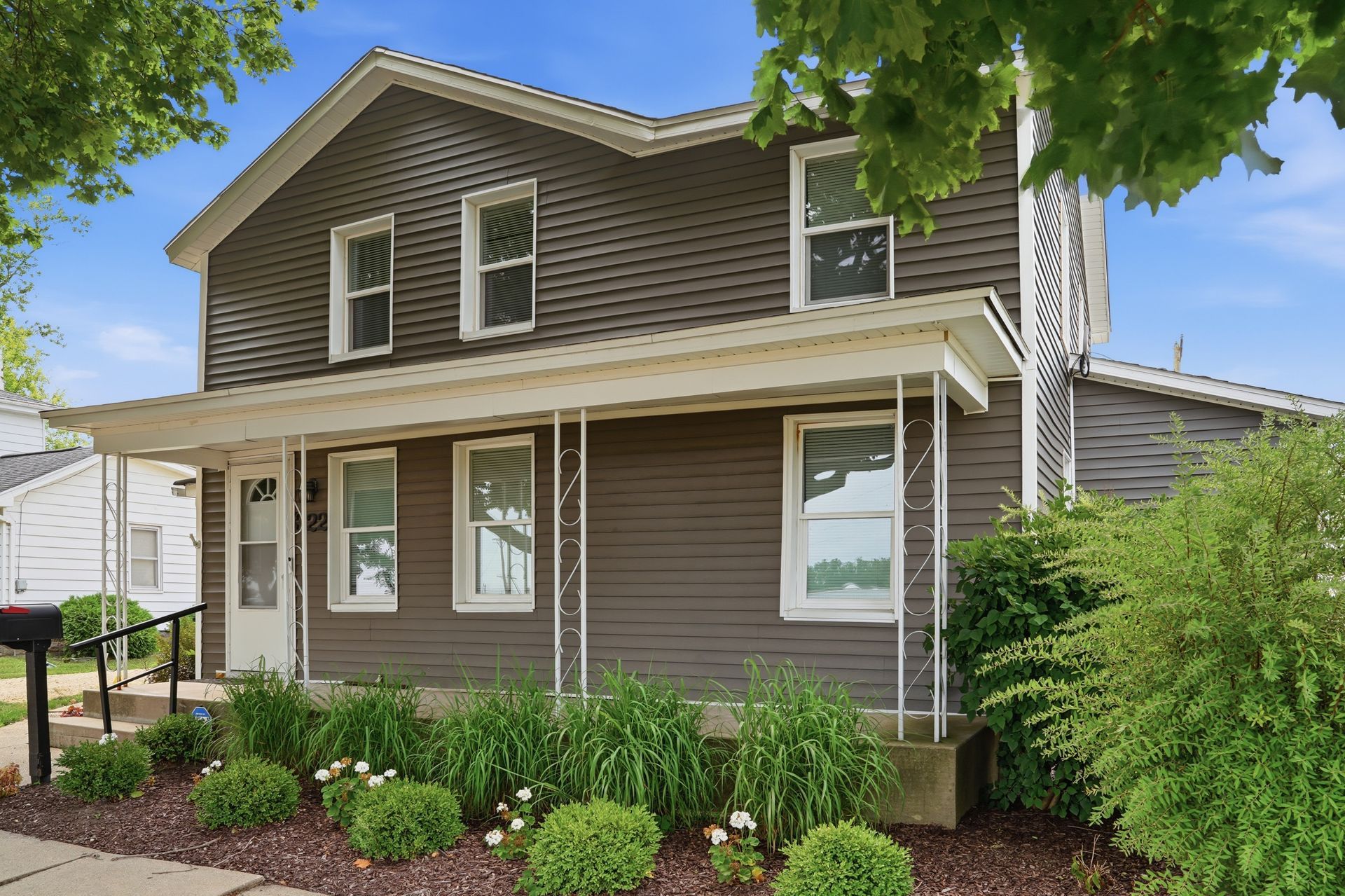 Two-story gray home with a covered front porch and garden beds