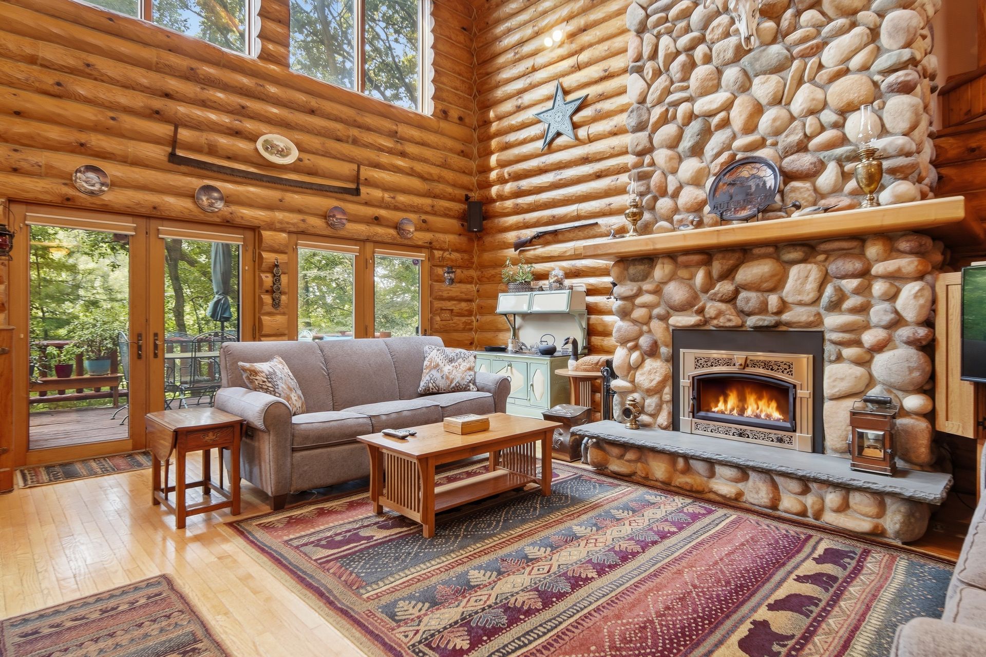 Log home living room with a stone fireplace and tall windows