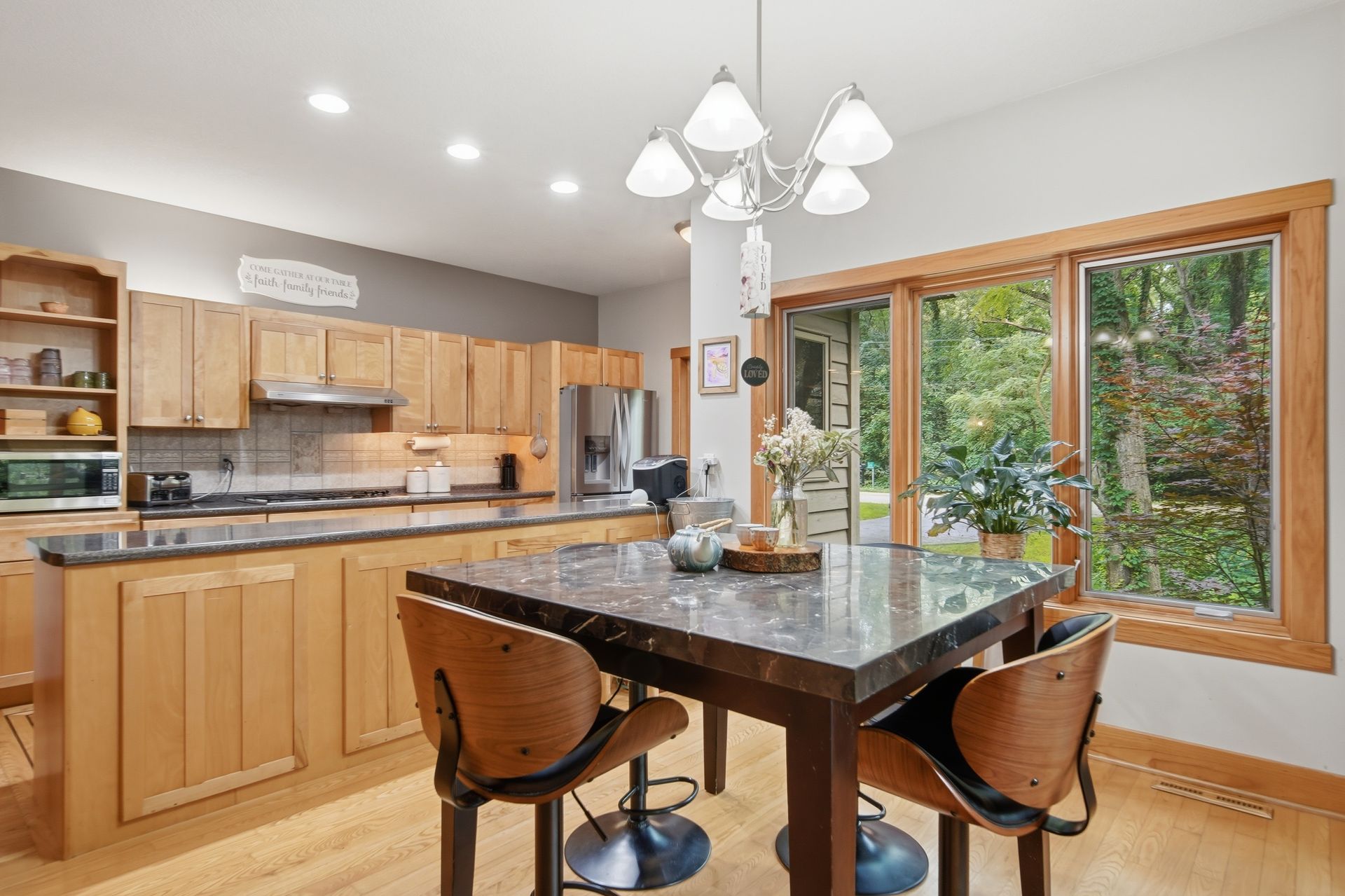Kitchen with wood cabinetry, a dark island and windows facing trees
