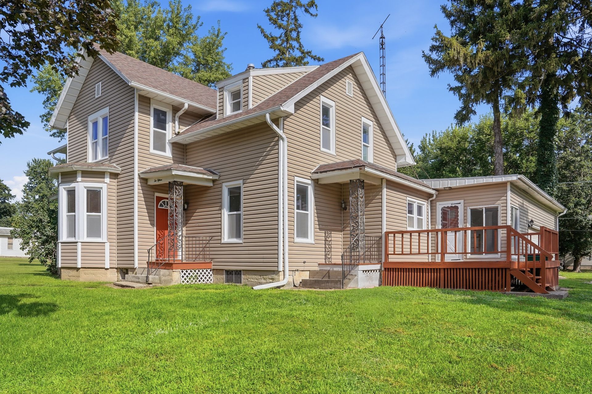 Two-story home with a side deck, green lawn and mature trees