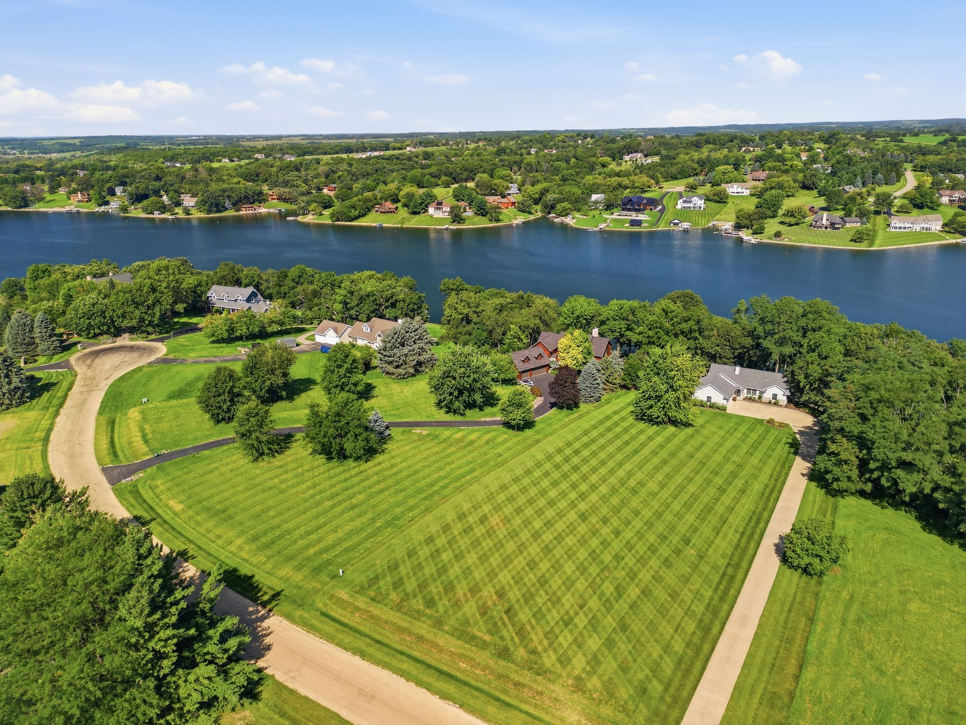 Aerial drone view of a waterfront property with a broad green lawn and surrounding countryside