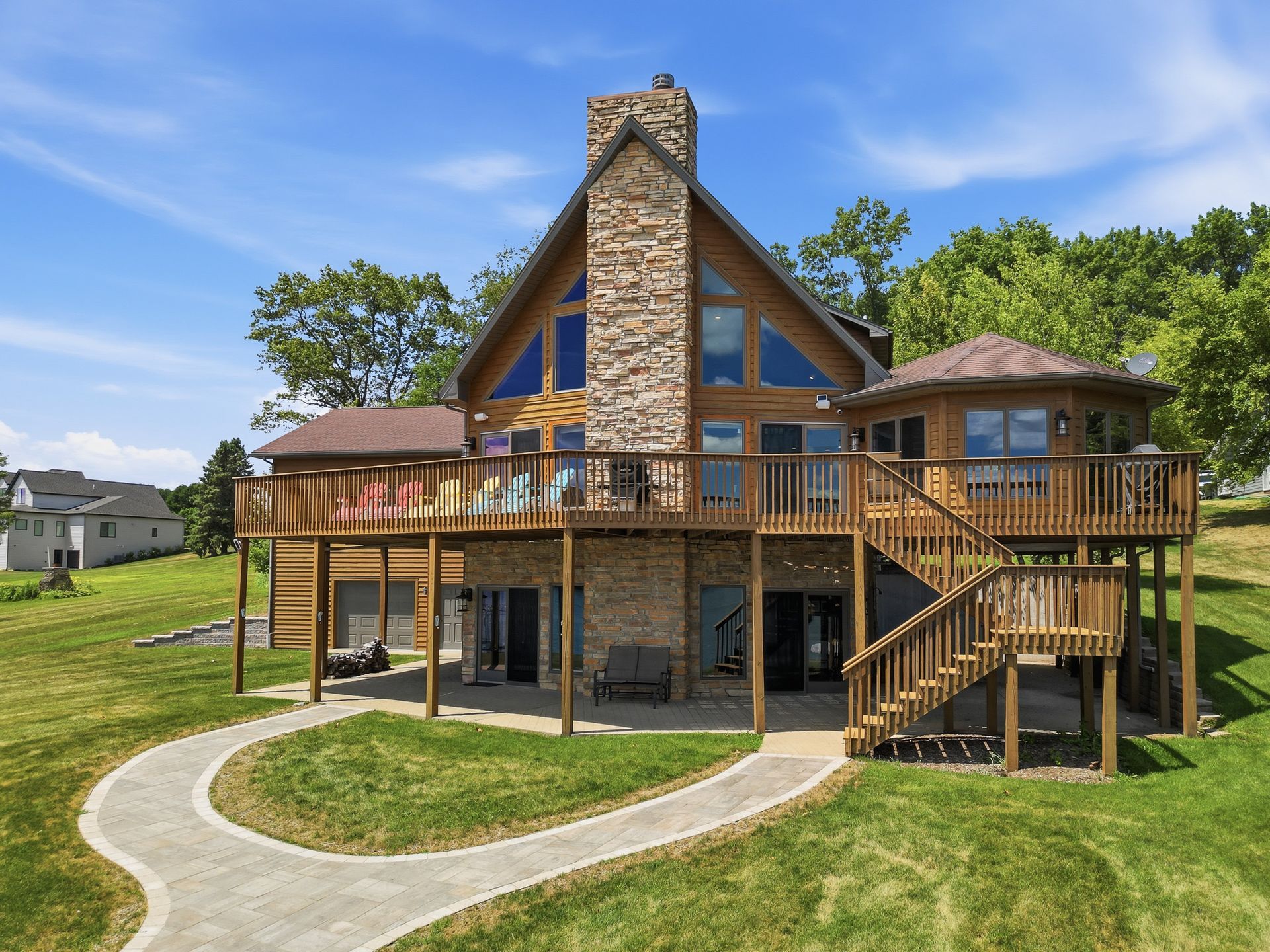 Home exterior with a wraparound deck, tall stone chimney and landscaped lawn