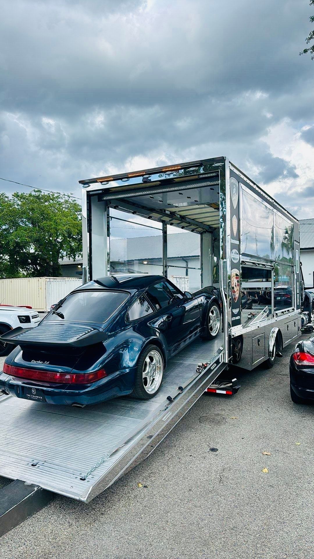A white Rolls-Royce Cullinan SUV secured on a flatbed tow truck parked on the shoulder of a highway under an overpass.