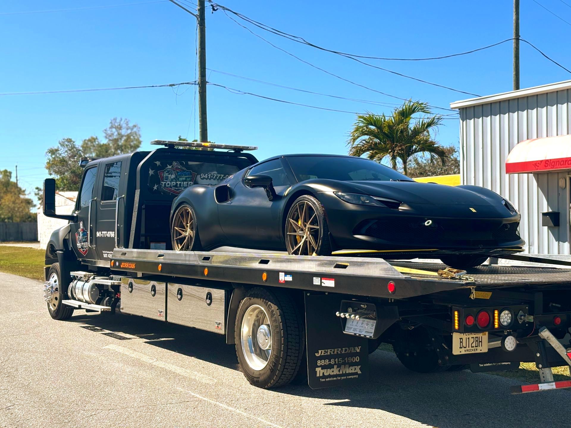 A black Ferrari sports car loaded onto a flatbed tow truck parked on a sunny street.