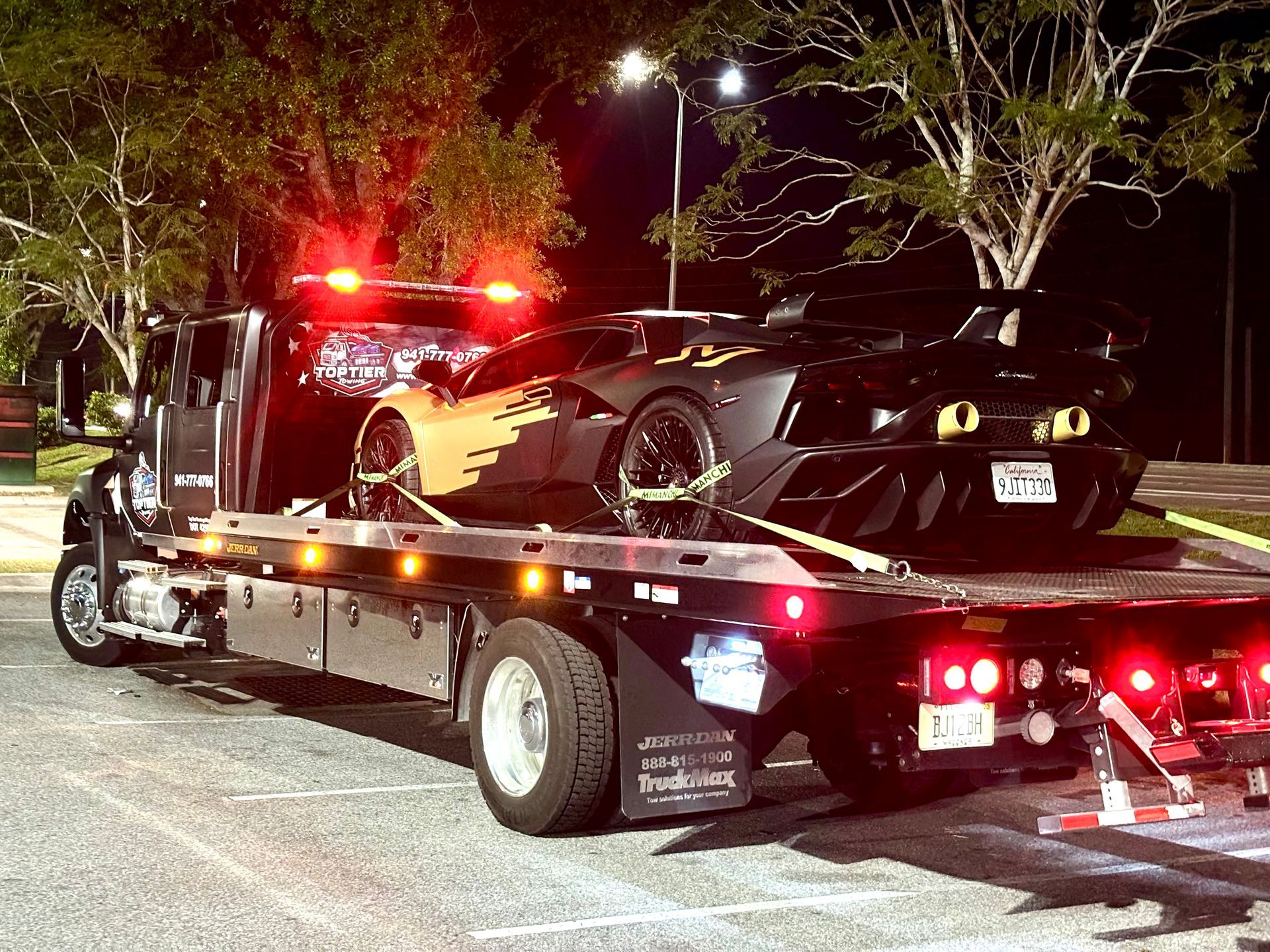 A black and yellow Lamborghini sports car secured on the back of a flatbed tow truck at night.