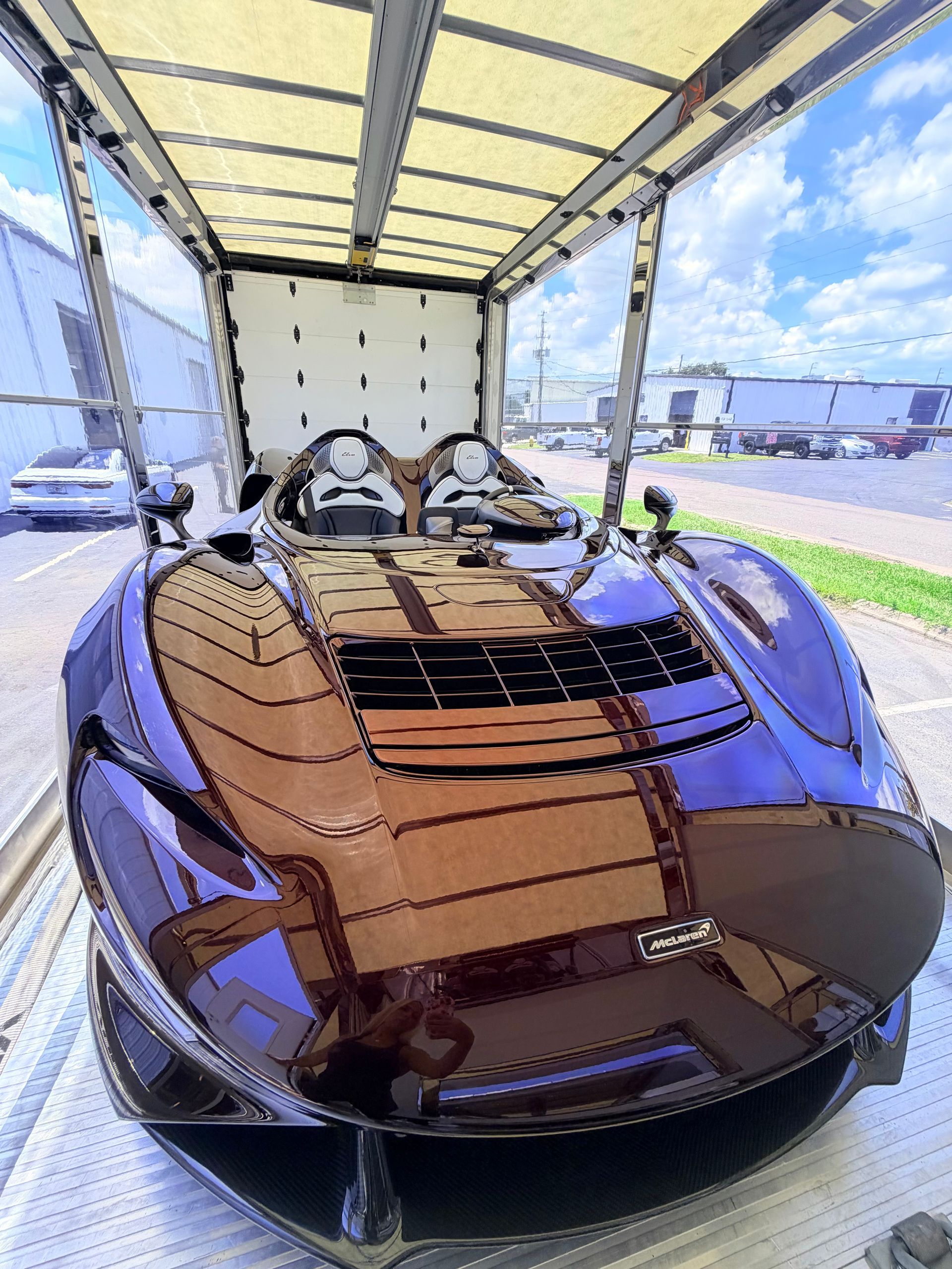 A black sports car loaded on the flatbed of a black tow truck parked on a gravel lot under sunny skies.