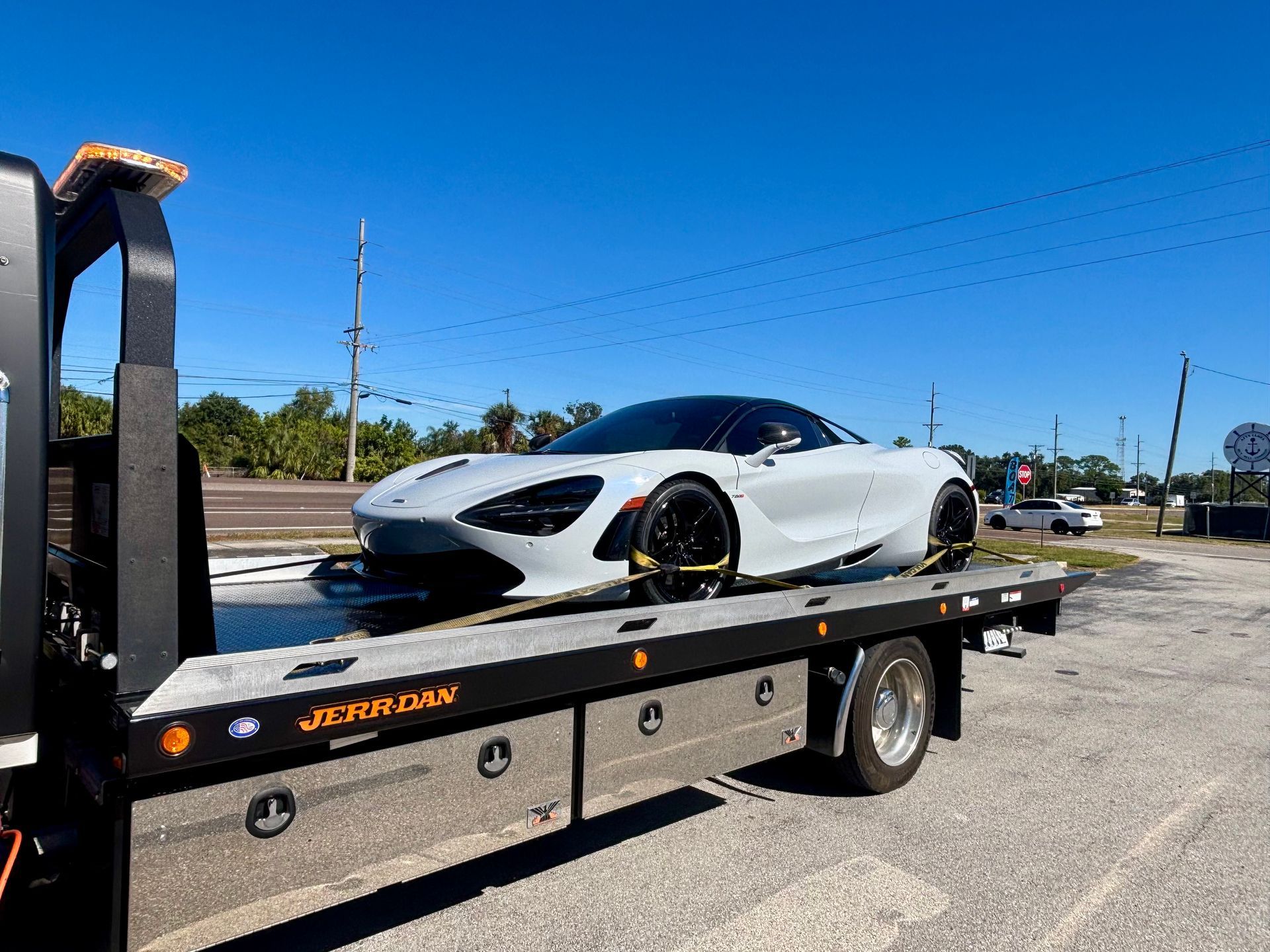 A white McLaren sports car secured on the flatbed of a tow truck on a sunny day.