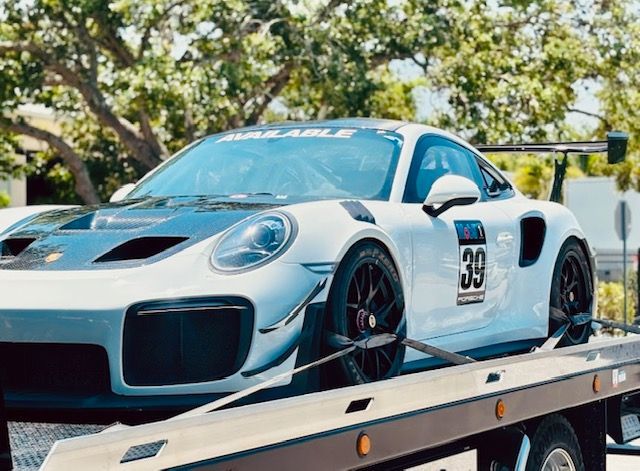 A white Porsche 911 GT2 RS race car with number 39 on the door is secured to the bed of a flatbed tow truck.