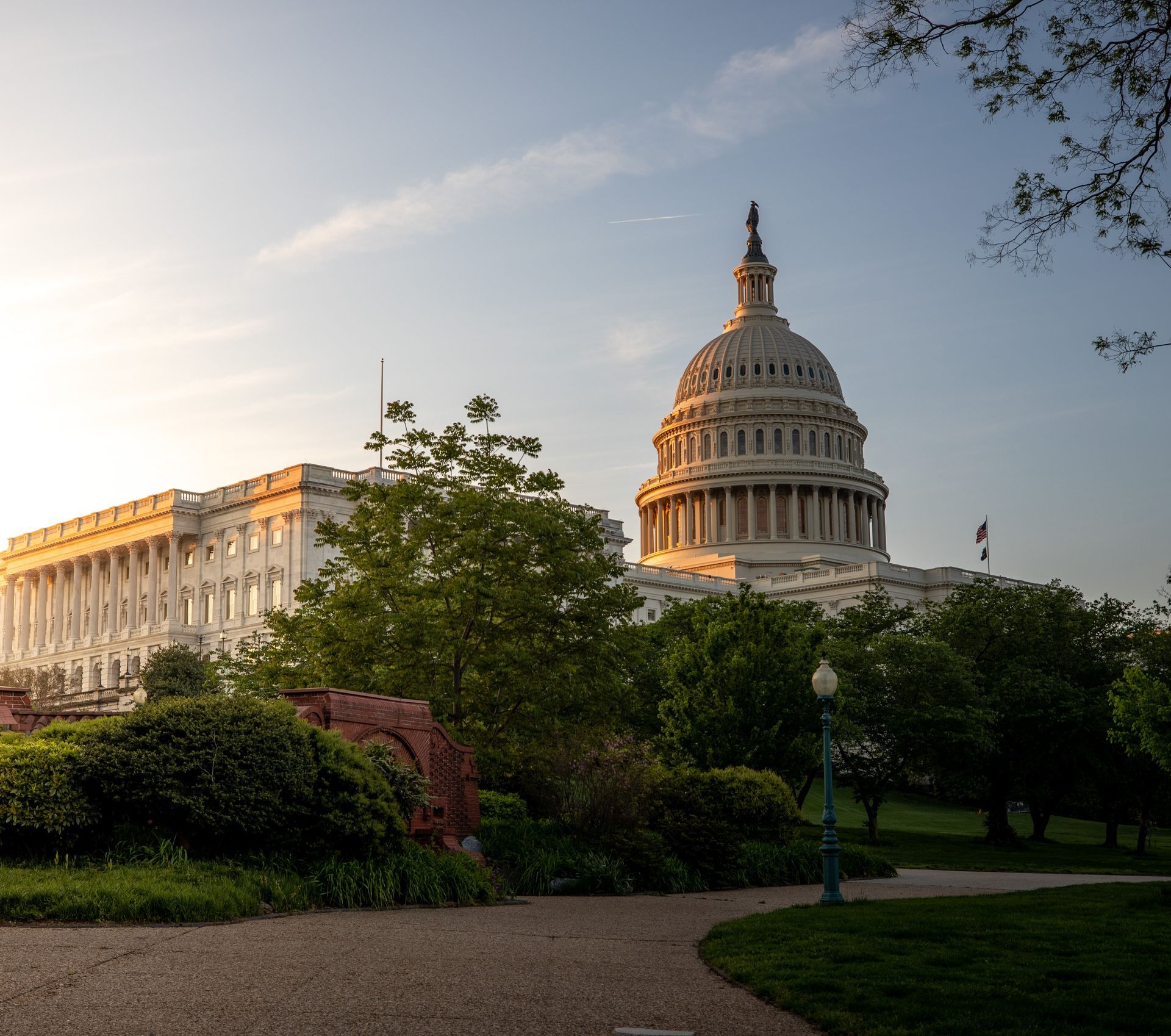 U.S. Capitol dome at sunset, framed by trees and a landscaped path in the foreground