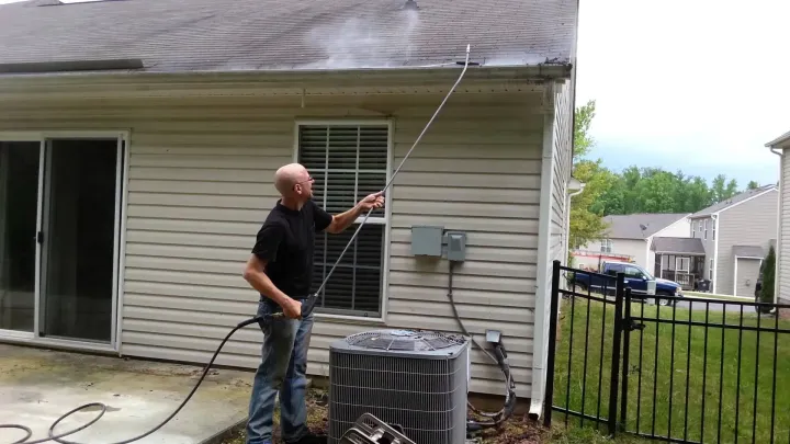 Man power washing house roof shingles