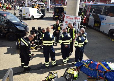 Emergency responders in dark uniforms gather near vehicles, including a bus and vans, with medical equipment visible.