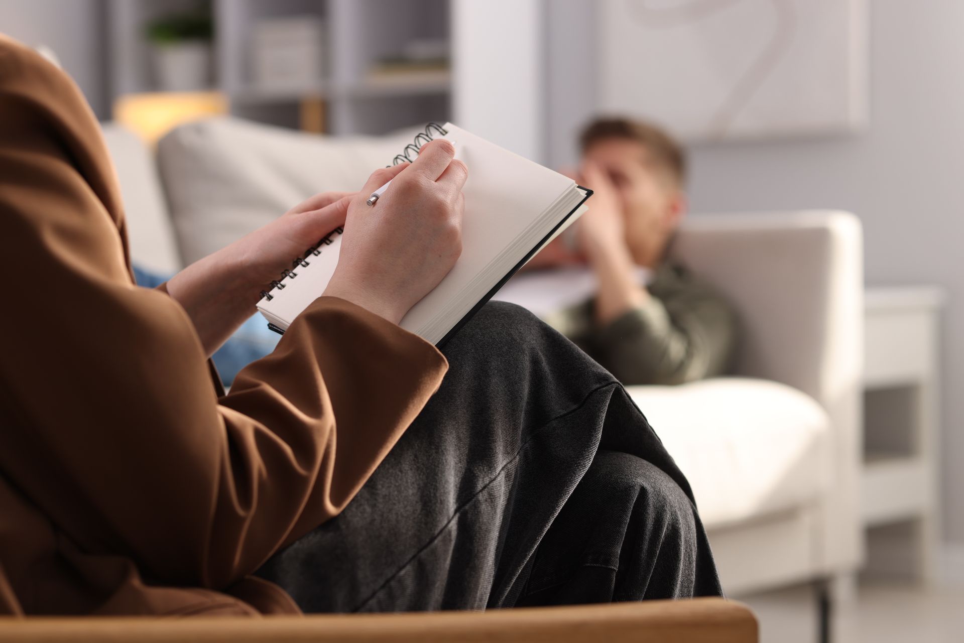 Clinical psychologist taking notes during a therapy session with a patient indoors.