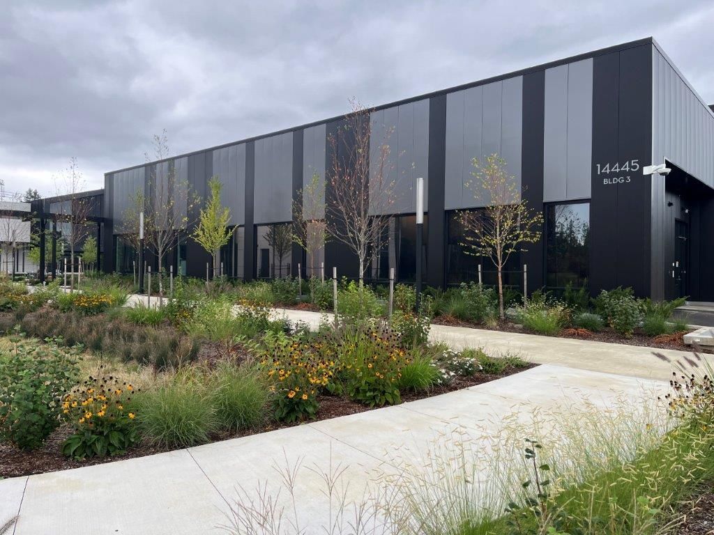 Modern office building with dark panels, landscaped garden, and a curved concrete walkway