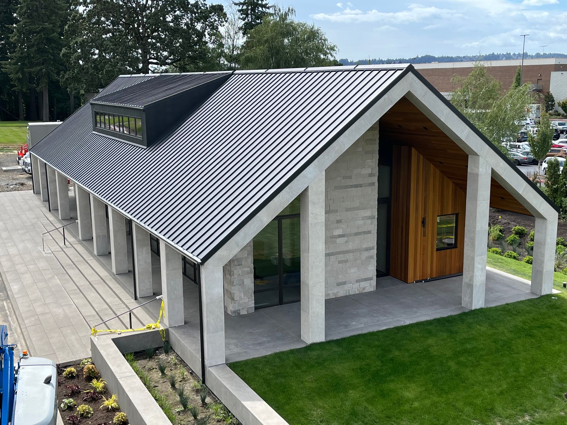 Modern white pavilion with a black sloped roof and green lawn on a paved site