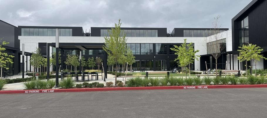 Modern building with large windows, trees, and a red curb in front under cloudy skies