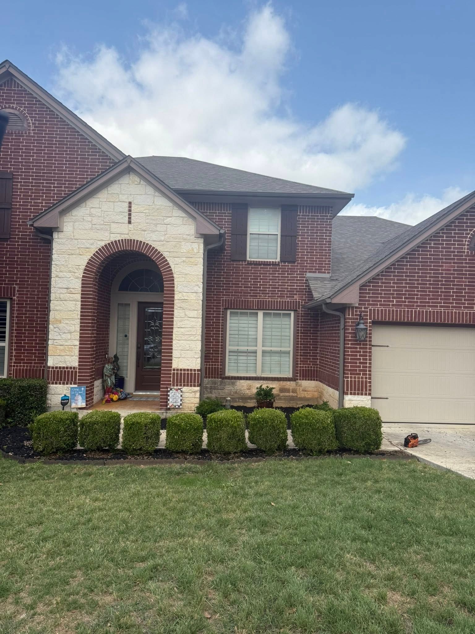 Brick house with stone trim, bushes, and garage door. Blue sky with clouds.