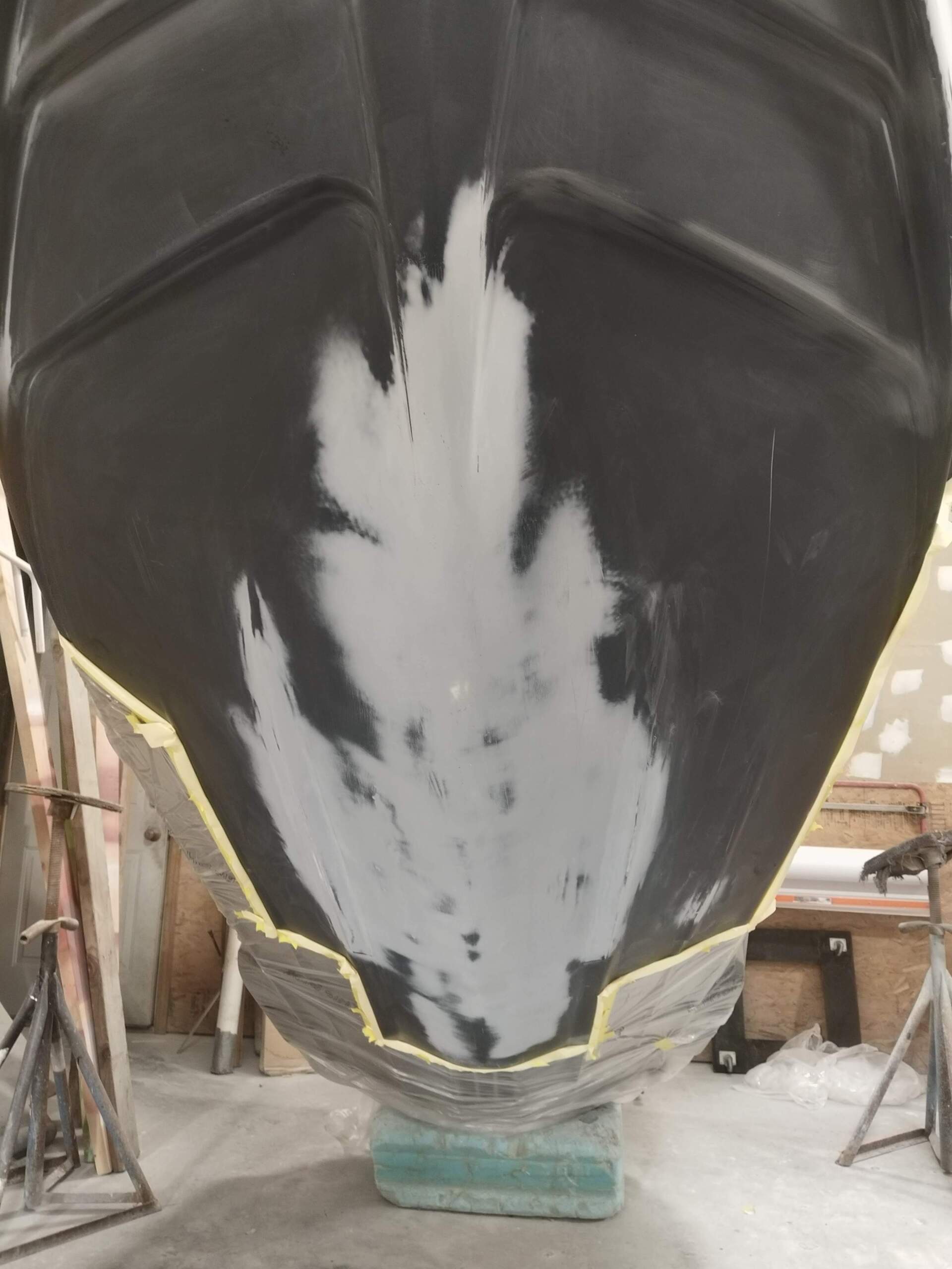 Close-up of a boat’s black hull with a white central stripe in a workshop or boatyard