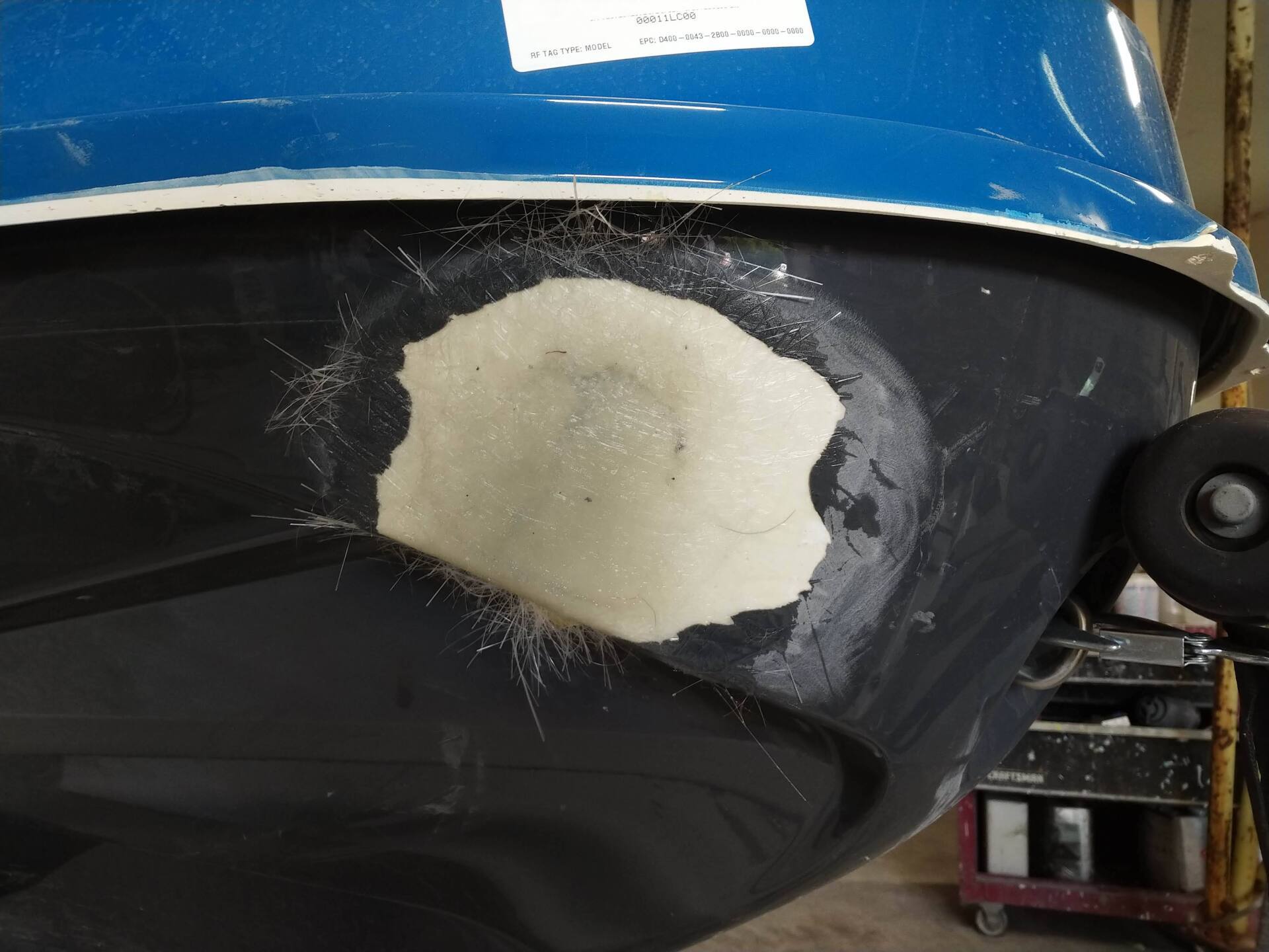 Close-up of a black boat hull with a white repair patch beneath a blue top edge.