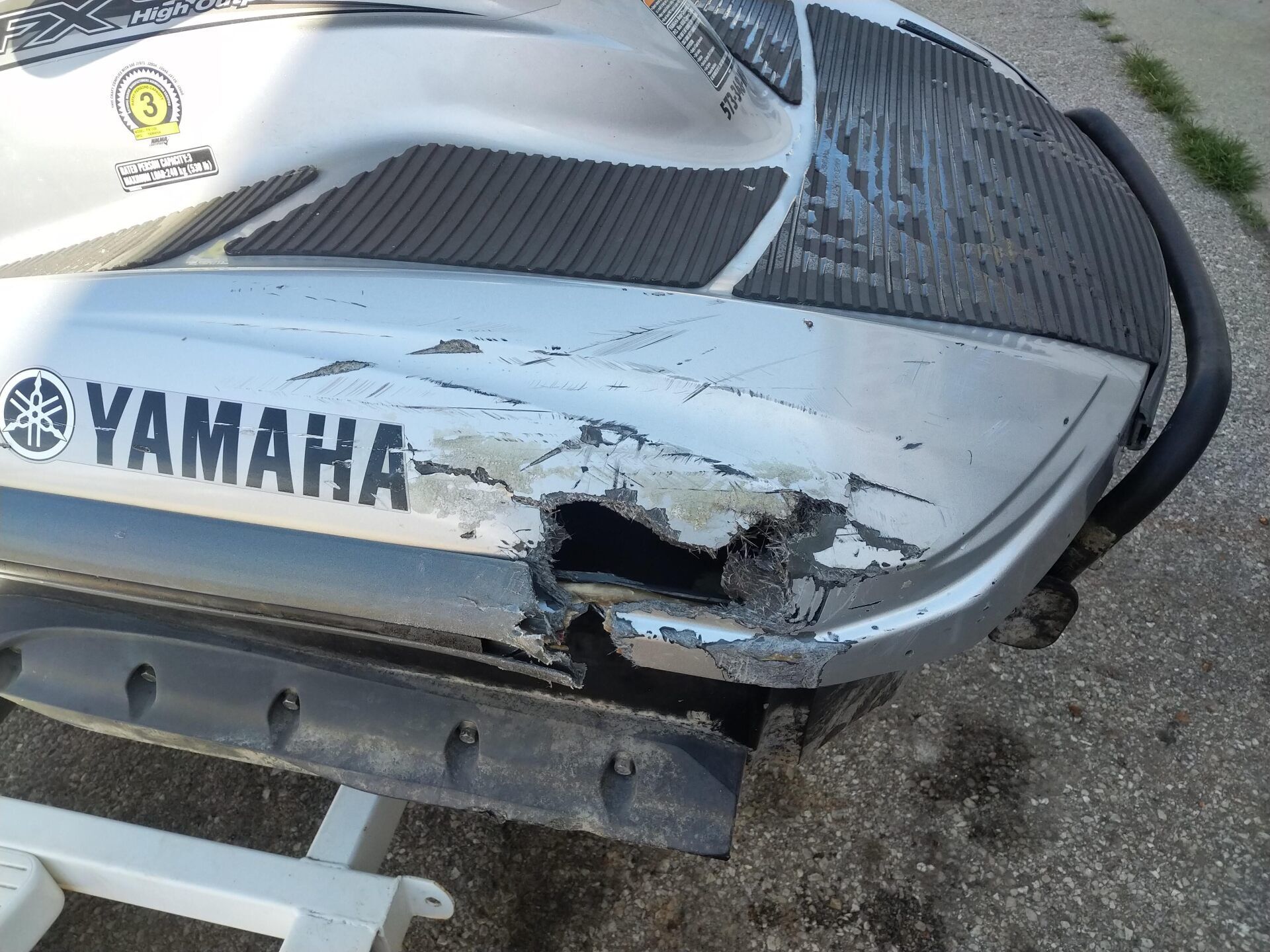 Damaged white Yamaha boat stern with a large hole and scraped hull on pavement