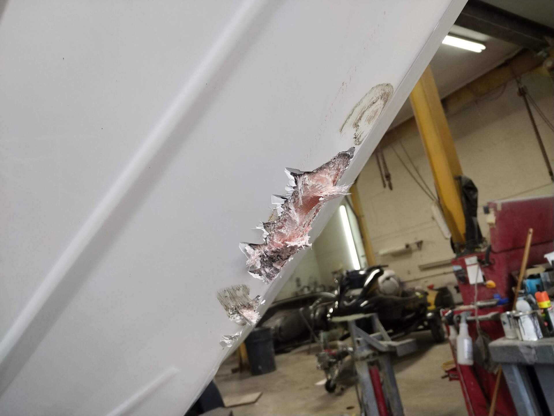 Close-up of a white car’s dented body panel with torn metal in a garage