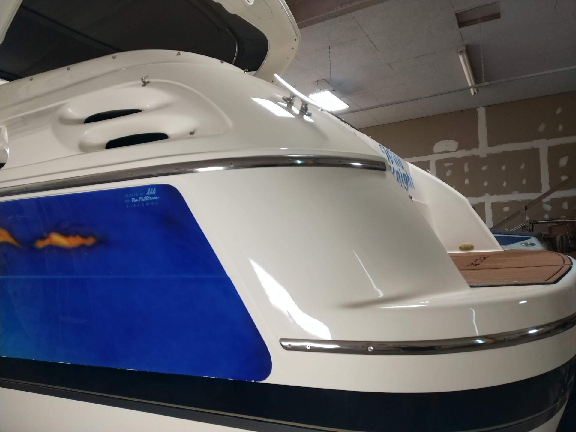 White boat stern with blue panel, docked indoors under a ceiling.