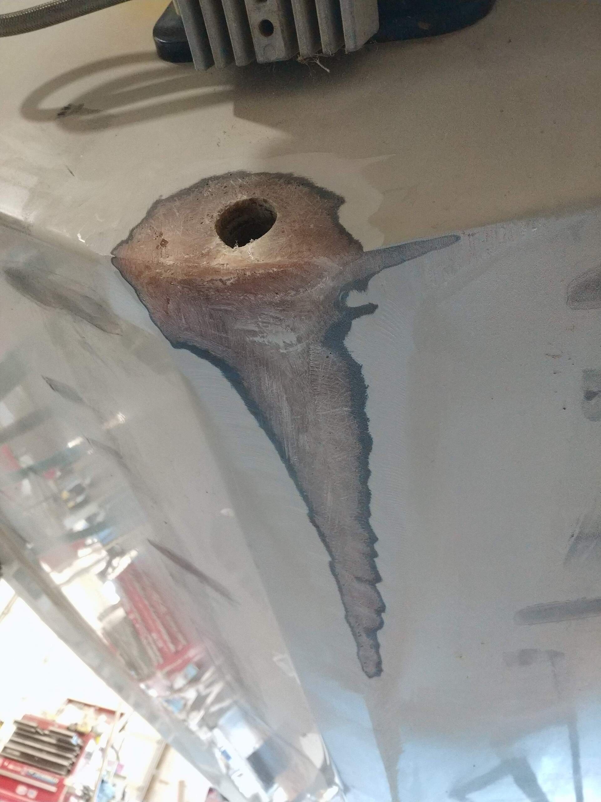 Close-up of a rusted metal surface with a drilled hole and a hanging wire on a light background
