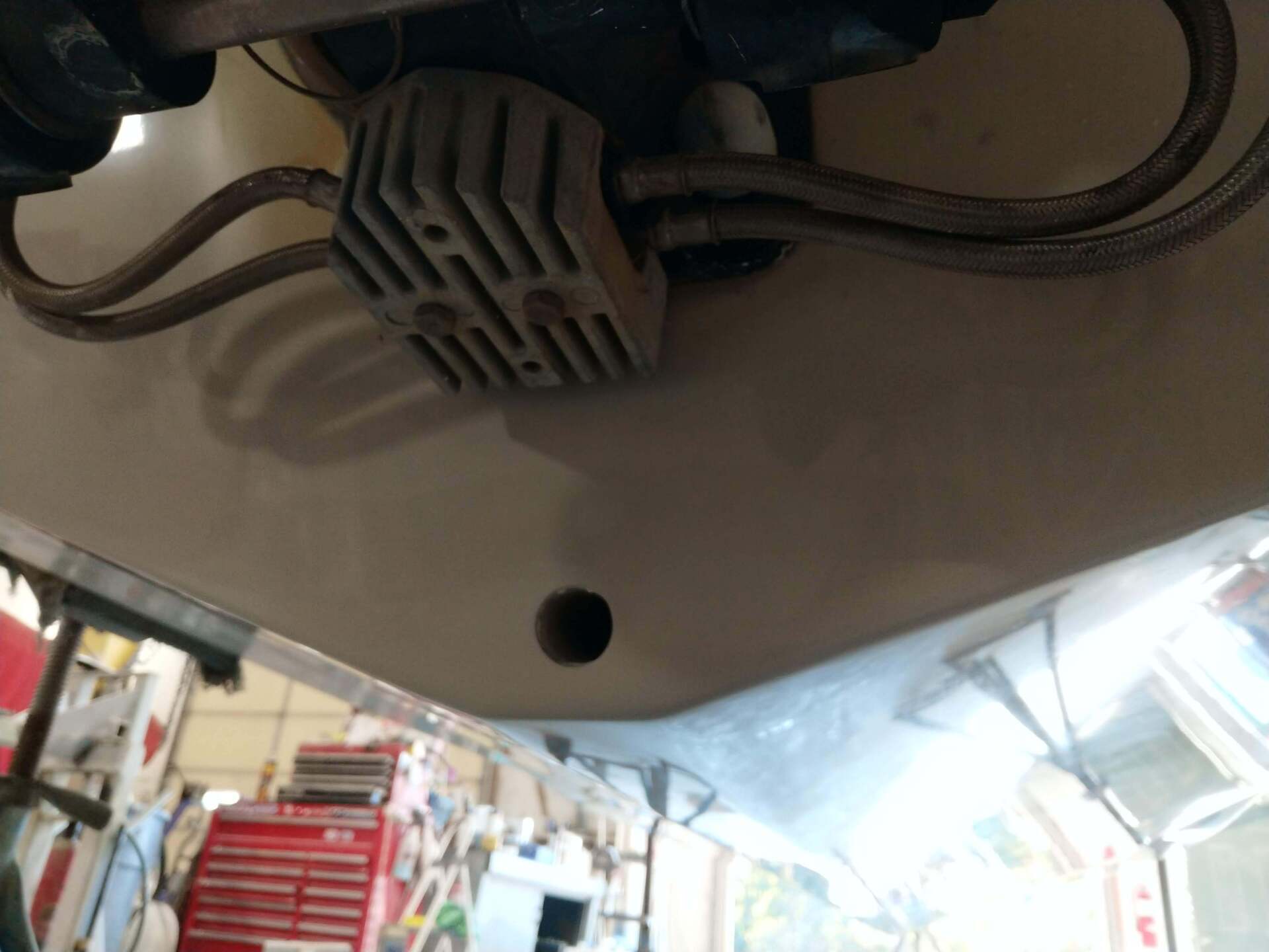 Close-up of a vehicle’s underside with a gray plastic cover and hanging cables at a workshop.