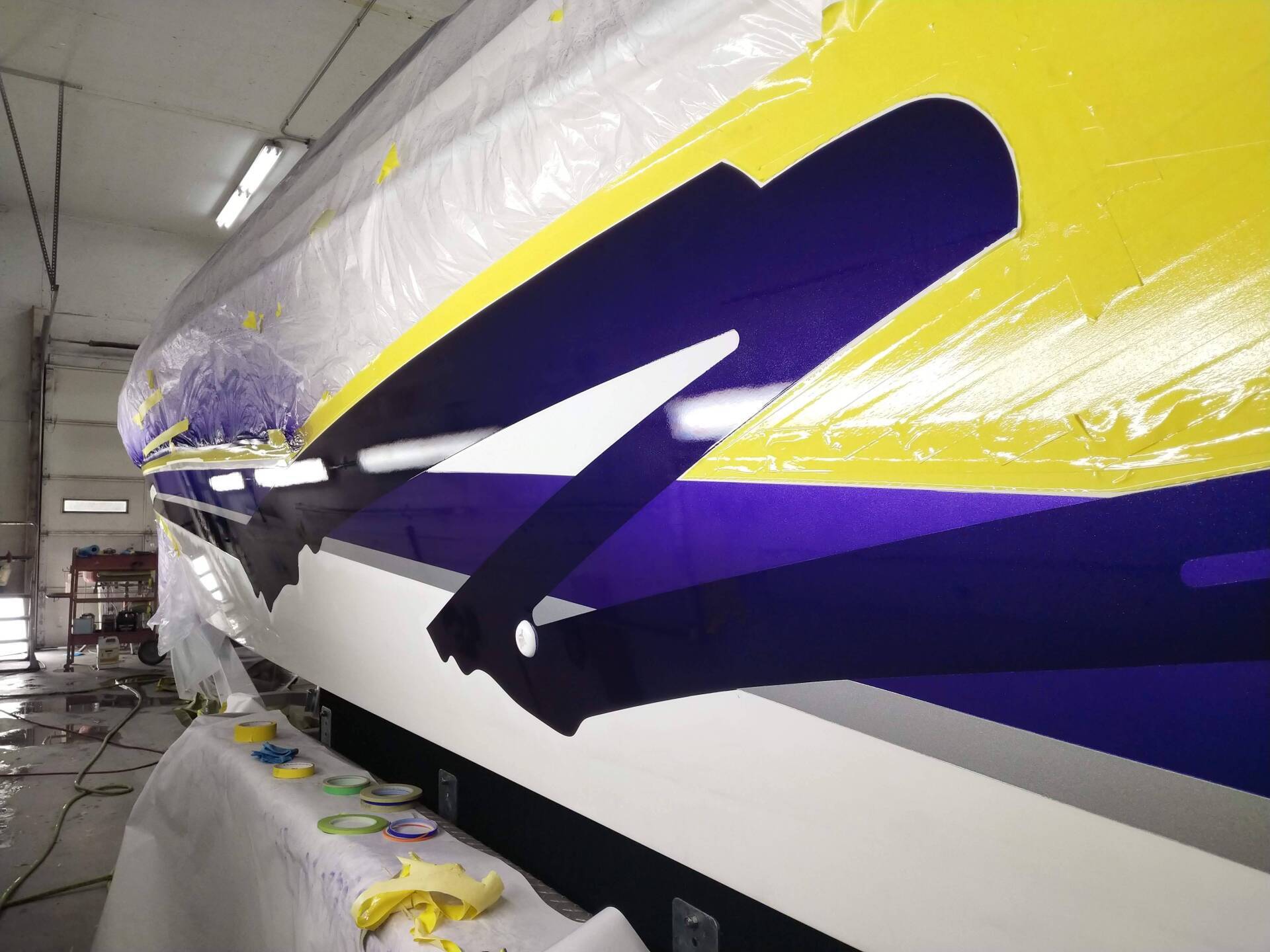 A yellow, purple, and white speedboat hull being painted in a workshop