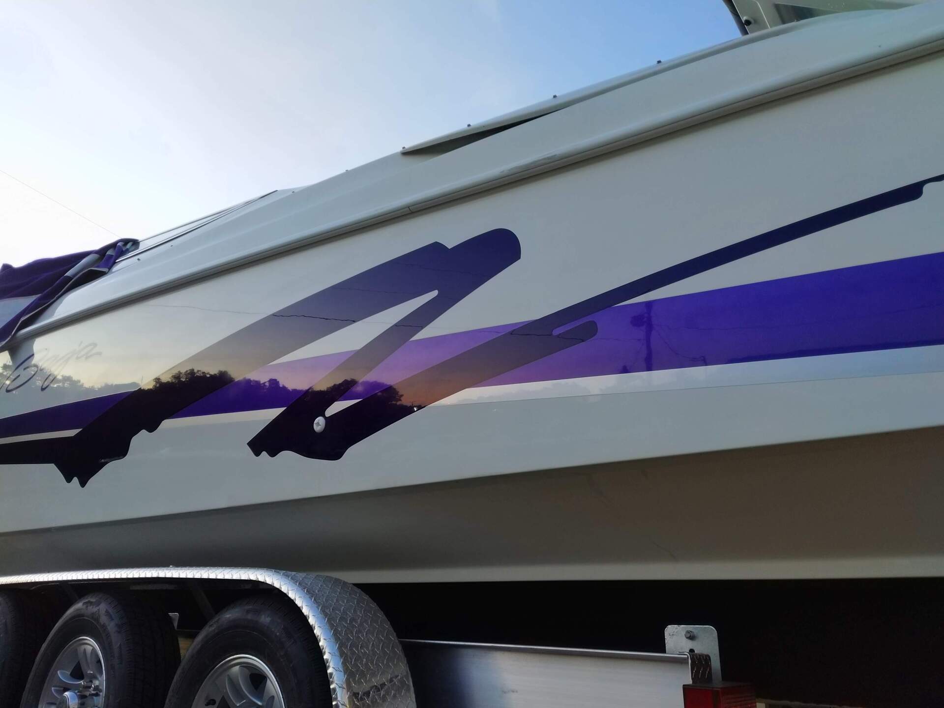 White boat with purple and black graphics on a trailer, viewed from the side.